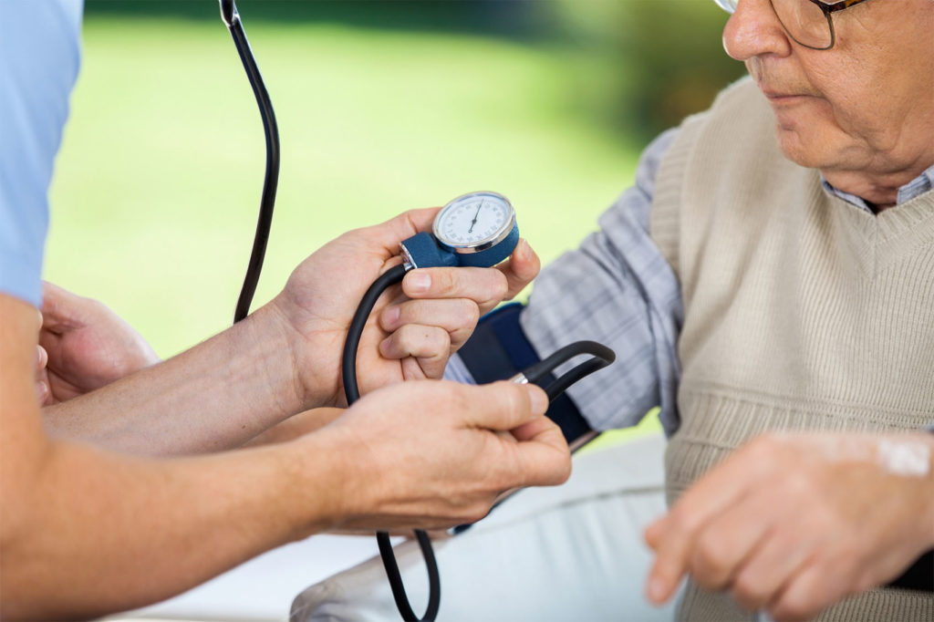 Cropped image of male caretaker measuring blood pressure of elderly man at nursing home